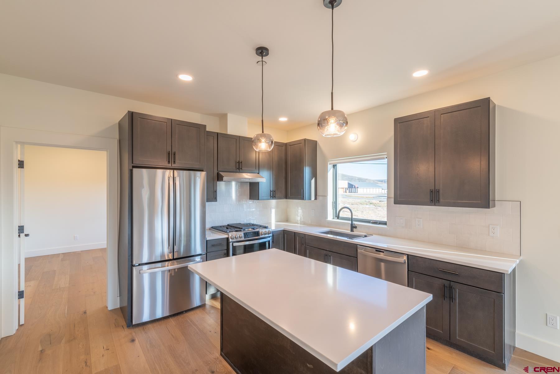 417 South Boulevard Street, Unit B Gunnison, CO 81230 - Photo 3 of 26 a kitchen with stainless steel appliances a refrigerator a sink a stove a kitchen island and couches with wooden floor