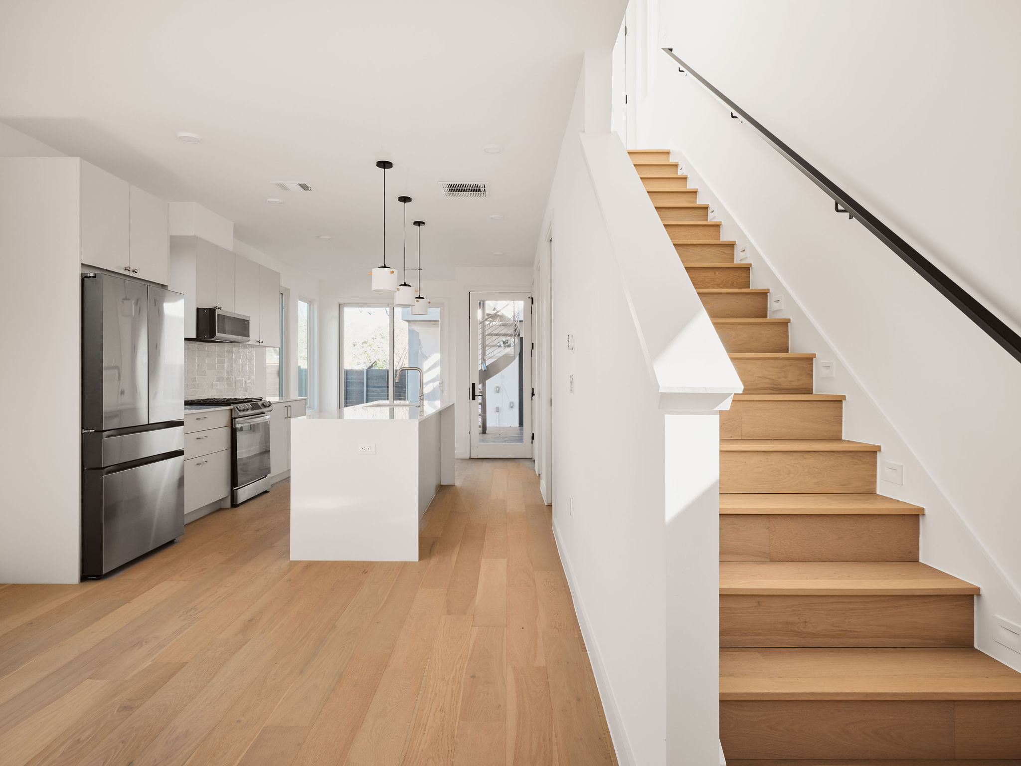 3209 Dolphin Drive, Unit 2 Austin, TX 78704 - Photo 14 of 28 Kitchen with stainless steel appliances, hanging light fixtures, white cabinets, an island with sink, and light wood finished floors