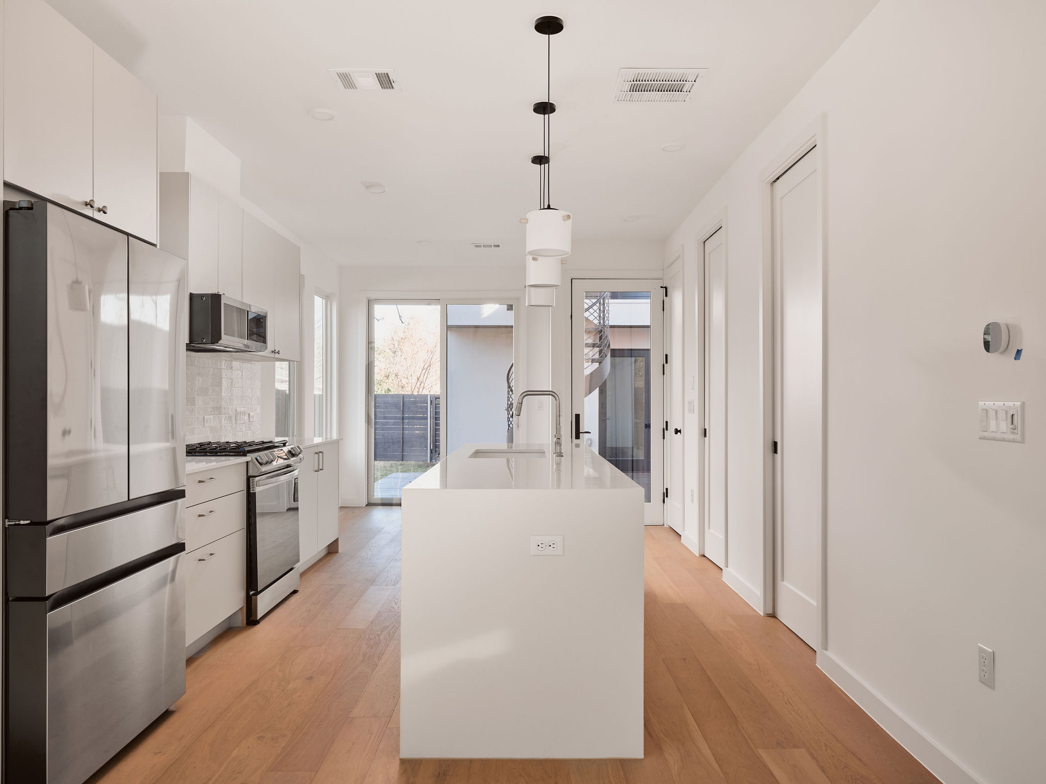3209 Dolphin Drive, Unit 2 Austin, TX 78704 - Photo 8 of 28 Kitchen with stainless steel appliances, white cabinets, decorative light fixtures, tasteful backsplash, and light wood-type flooring