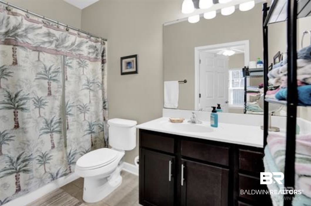 430 West Fort Morgan Road Gulf Shores, AL 36542 - Photo 12 of 27 Bathroom featuring a shower with a privacy curtain, a white toilet, and a vanity with a dark wood-finish cabinet, white countertop, and integrated sink