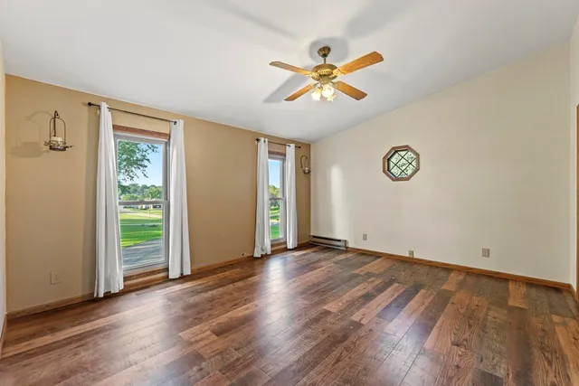 an empty room with wooden floor chandelier fan and windows