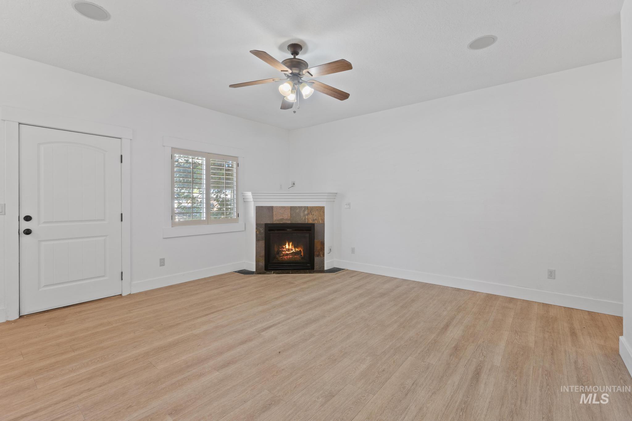 5271 West Morris Hill Road Boise, ID 83706 - Photo 11 of 31 Unfurnished living room featuring a tile fireplace, light wood-style flooring, and a ceiling fan