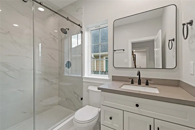 a bathroom with a toilet a sink a mirror a shower and vanity