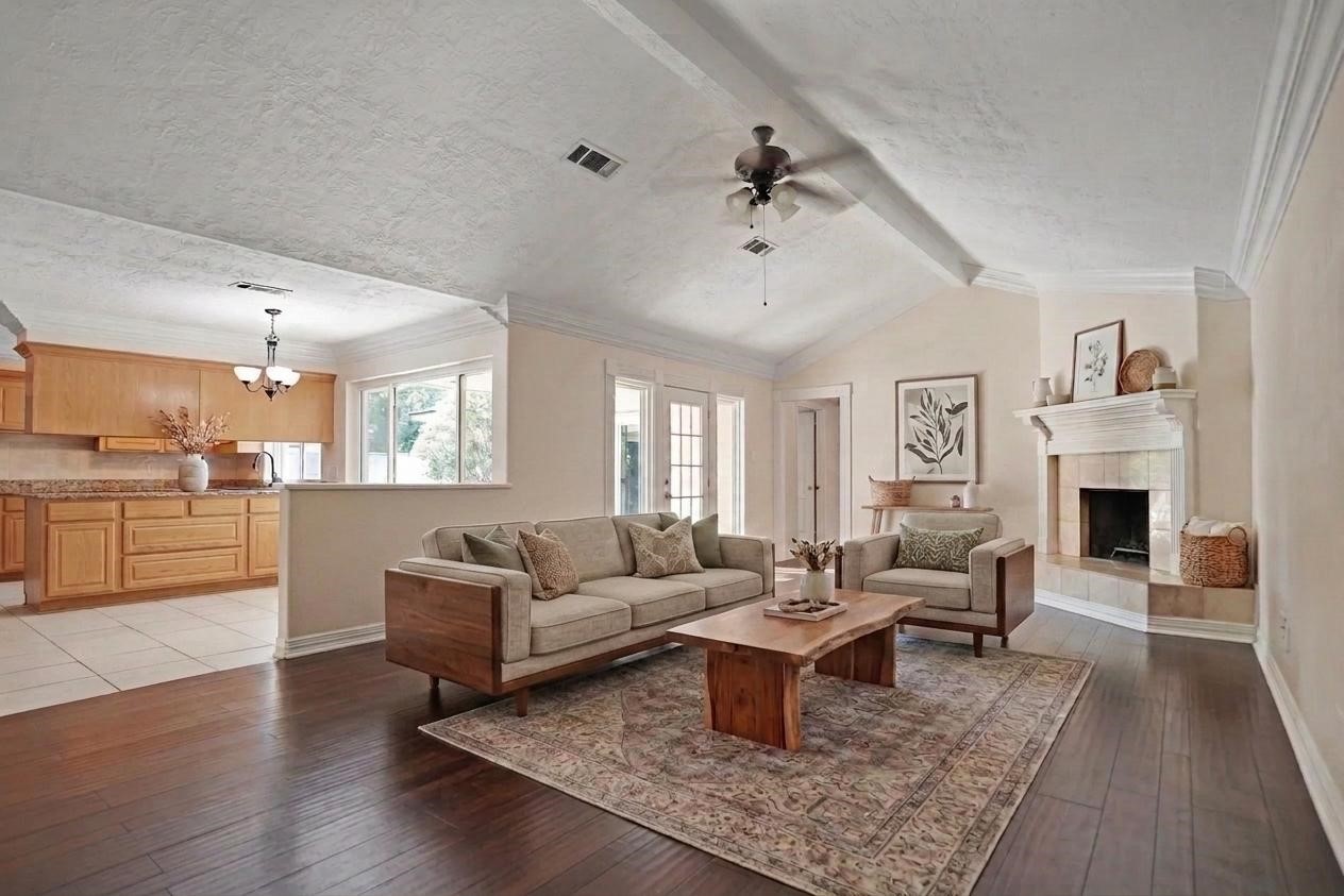 17119 Mellow Ridge Drive Spring, TX 77379 - Photo 4 of 32 This photo showcases a spacious living room with high ceilings and a ceiling fan. The room features a cozy fireplace, large windows for natural light, and an open layout that flows into the kitchen area with wooden cabinetry. The space is elegantly furnished, highlighting the warm wood flooring and inviting atmosphere.