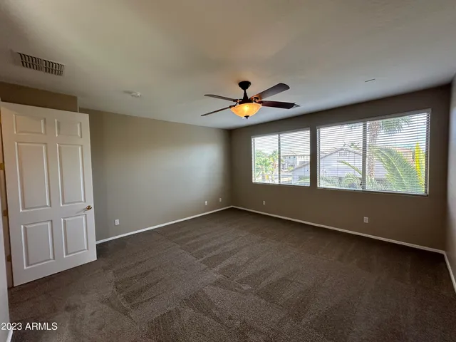 a view of n empty room with chandelier fan and window
