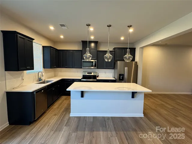 a large kitchen with stainless steel appliances a large counter top a stove a sink and a refrigerator