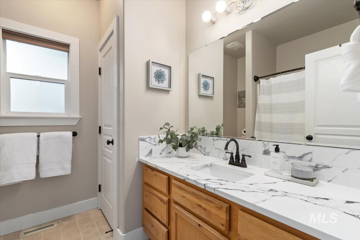 10462 West Lanktree Gulch Road Star, ID 83669 - Photo 25 of 48 Bathroom featuring a single-sink vanity with a white countertop and integrated backsplash, wood-finish cabinetry, and a dark-finish faucet