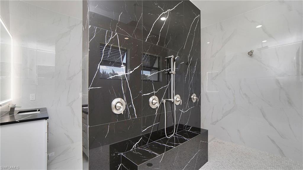 2343 Oil Well Road Naples, FL 34120 - Photo 20 of 46 Luxurious shower featuring black marbled wall tiling with white veining, a built-in shower bench, and a brushed nickel shower system