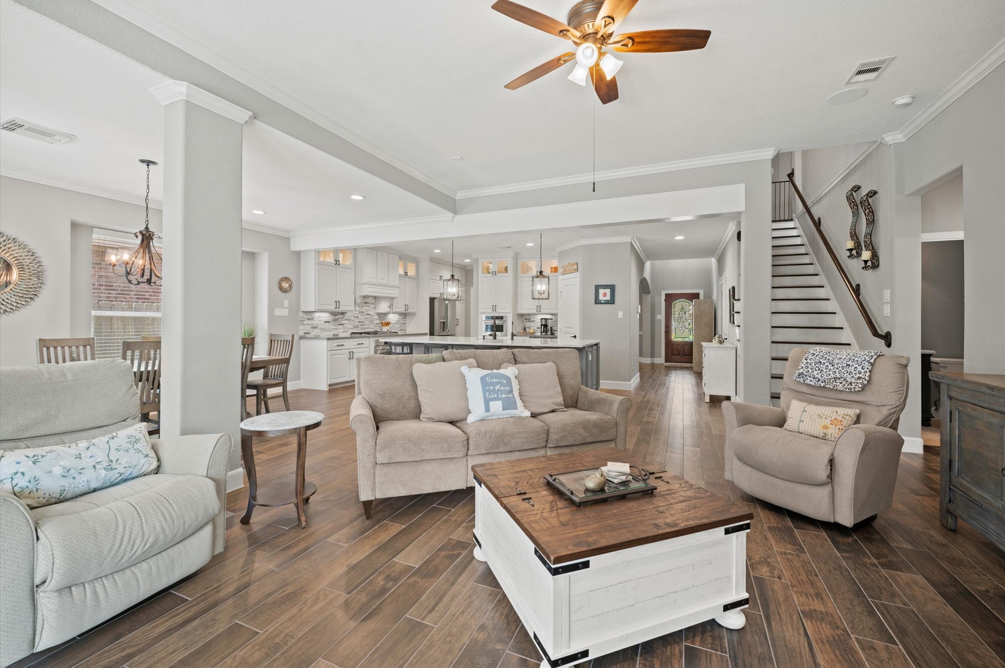 9507 Empress Crossing Drive Spring, TX 77379 - Photo 19 of 50 This open-concept living space features a cozy seating area with neutral-toned furniture, a stylish ceiling fan, and wood-look flooring. The kitchen has modern appliances, a large island, and ample cabinetry. A staircase leads to the upper level, and a dining area is nearby, creating a welcoming environment.