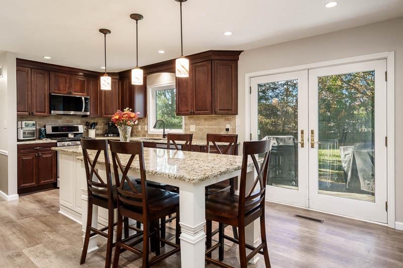 11948 Southgate Road Roscoe, IL 61073 - Photo 19 of 73 a kitchen with stainless steel appliances granite countertop a stove a refrigerator a microwave a sink a dining table and chairs with wooden floor