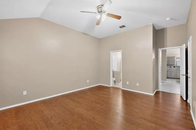 a view of an empty room with wooden floor and a kitchen