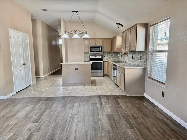 a kitchen with stainless steel appliances granite countertop a sink a microwave oven a refrigerator and white cabinets with wooden floor