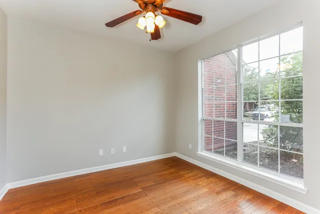 an empty room with wooden floor fan and windows