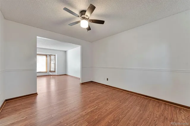 an empty room with wooden floor chandelier fan and windows