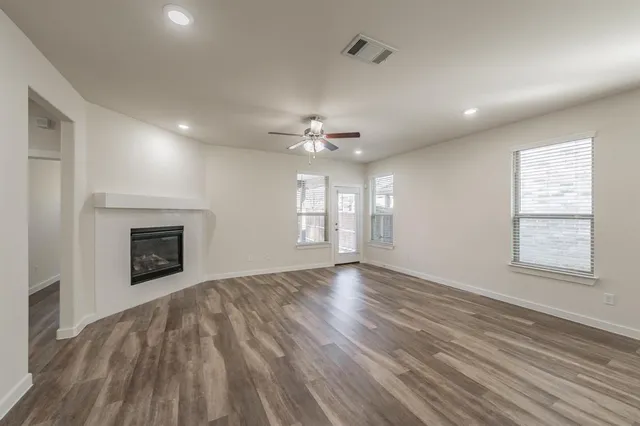 a view of an empty room with wooden floor fireplace and a window