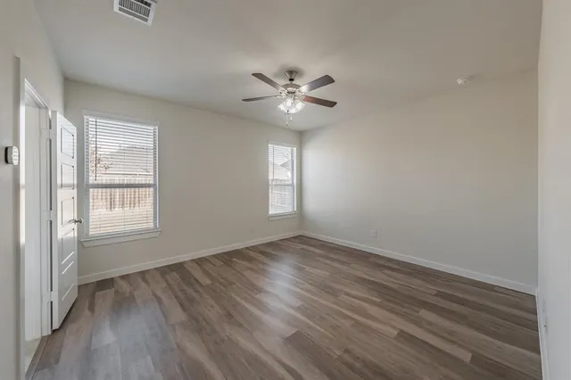 an empty room with wooden floor ceiling fan and windows