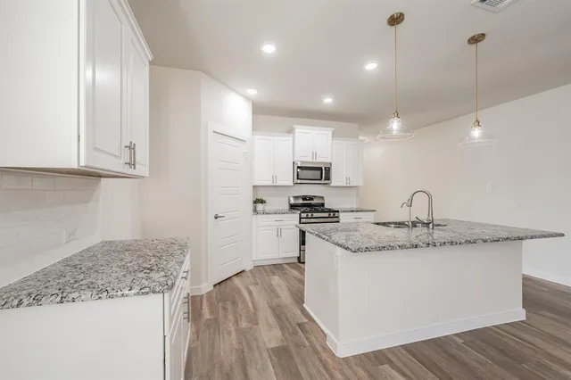 a kitchen with stainless steel appliances granite countertop a sink a stove a refrigerator and island with wooden floor