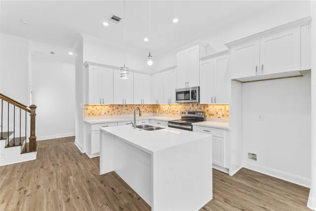 a kitchen with a sink a stove a refrigerator and white cabinets with wooden floor