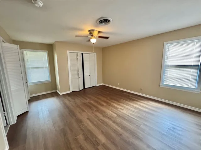 an empty room with wooden floor chandelier fan and windows