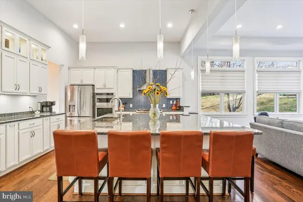 a kitchen with stainless steel appliances granite countertop a coffee maker a sink a stove and white cabinets with wooden floor