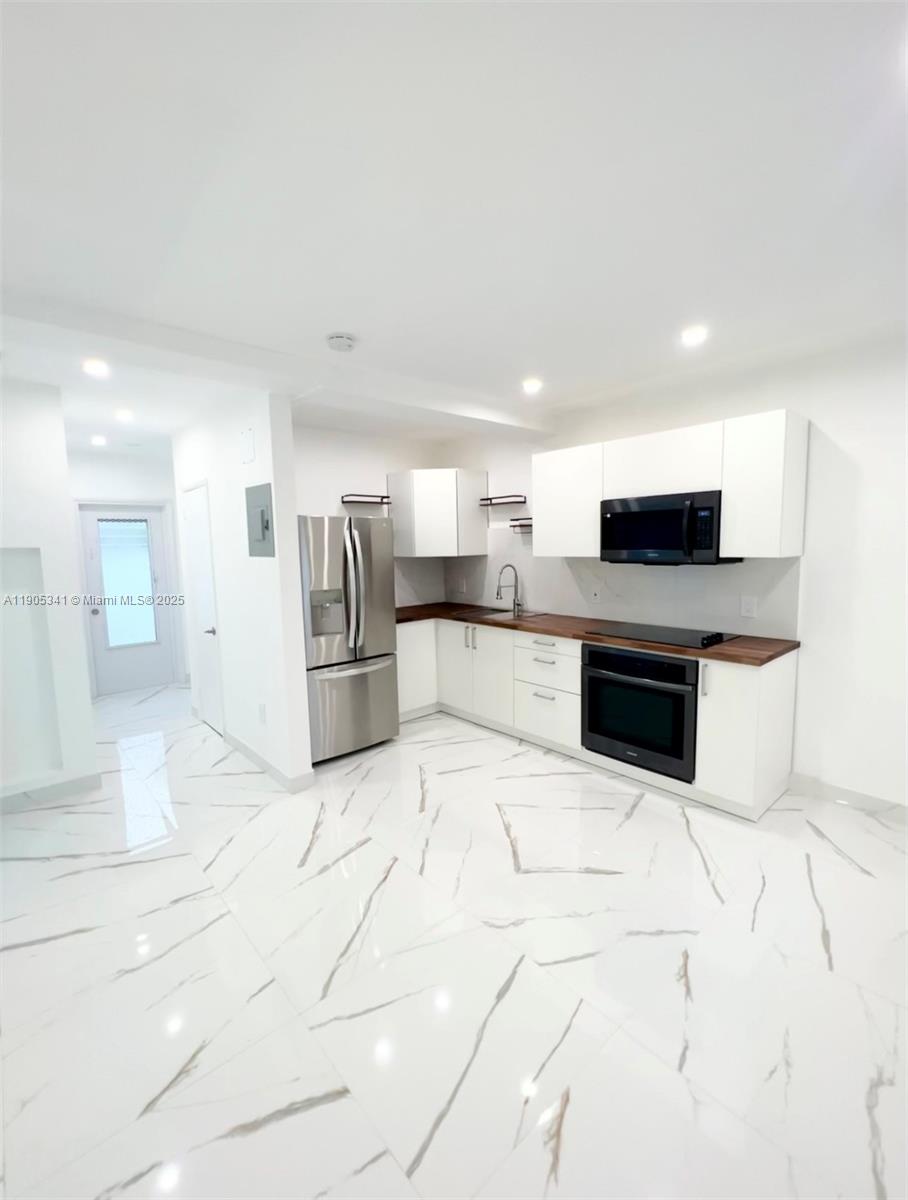 7300 Byron Avenue, Unit 10 Miami Beach, FL 33141 - Photo 4 of 10 a large white kitchen with stainless steel appliances kitchen island granite countertop a stove top oven and a sink