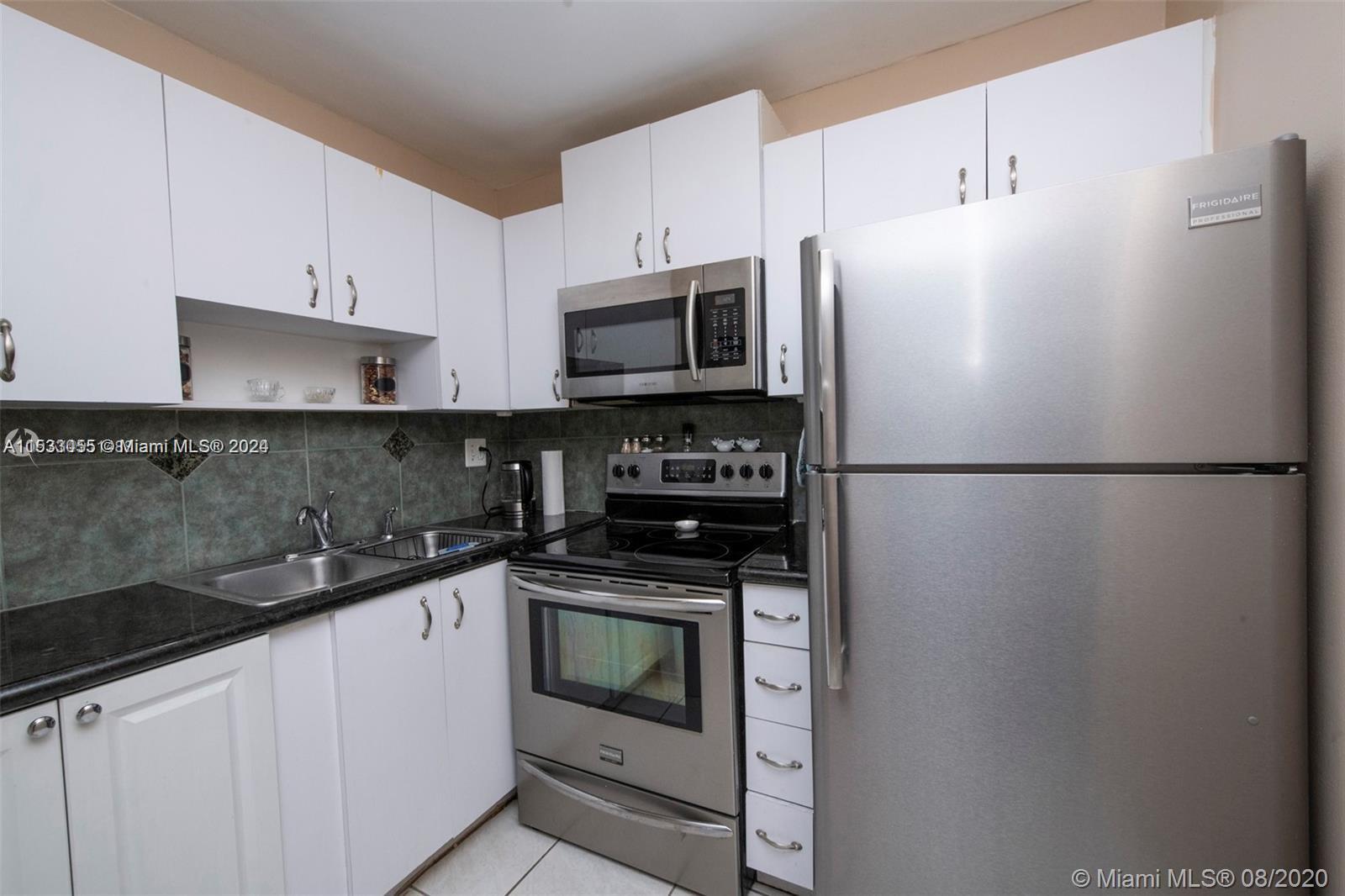 a white kitchen with stainless steel appliances granite countertop a refrigerator sink and stove
