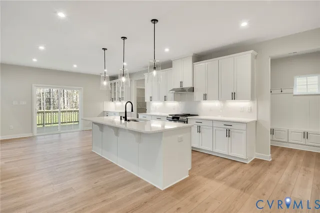 a kitchen with stainless steel appliances granite countertop a sink a stove a refrigerator and white cabinets with wooden floor