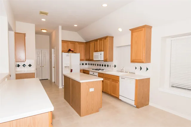 a large white kitchen with stainless steel appliances kitchen island granite countertop a refrigerator a sink dishwasher and white cabinets with wooden floor