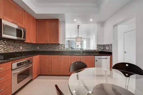 a kitchen with stainless steel appliances granite countertop a stove a sink a microwave a refrigerator a dining table and chairs with wooden floor