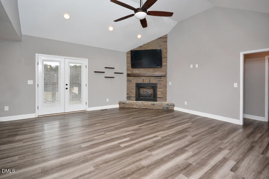 3082 East Thollie Green Road Stem, NC 27581 - Photo 5 of 45 an empty room with wooden floor a ceiling fan a fireplace and windows