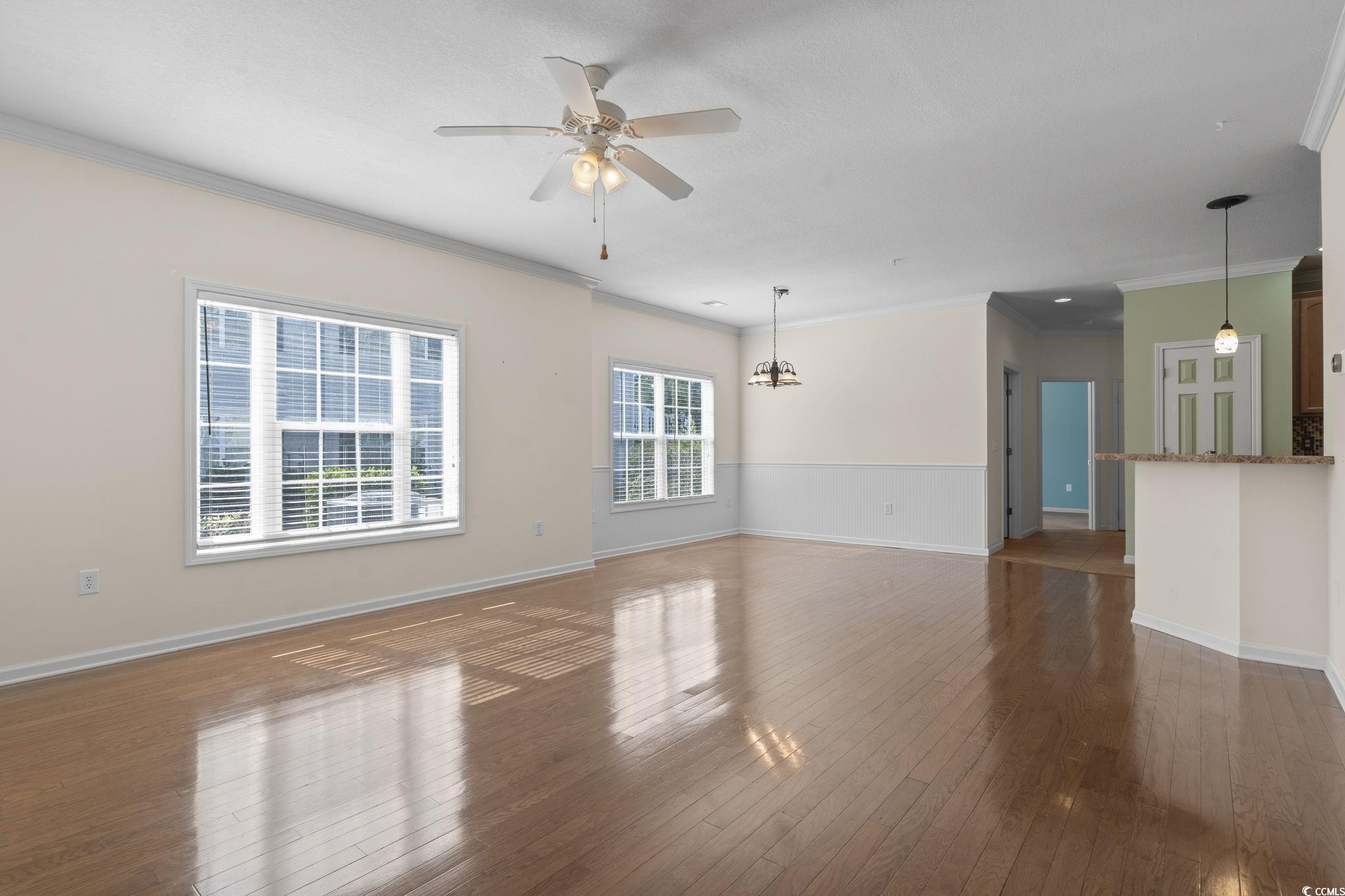 237 Moonglow Circle, Unit 102 Murrells Inlet, SC 29576 - Photo 15 of 35 Unfurnished living room featuring crown molding, dark wood-style flooring, a ceiling fan, and a chandelier