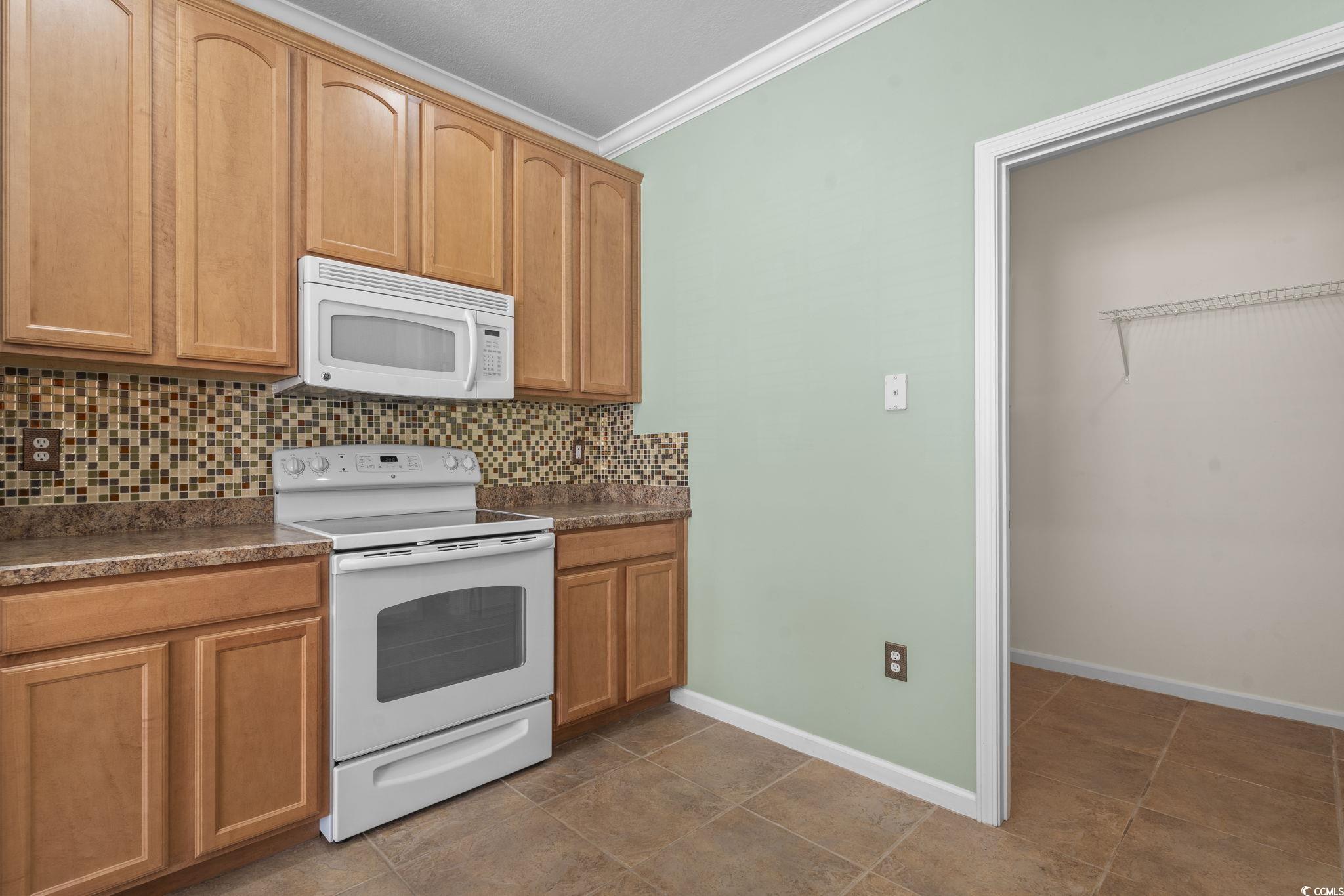 237 Moonglow Circle, Unit 102 Murrells Inlet, SC 29576 - Photo 6 of 35 Kitchen featuring white appliances, dark countertops, backsplash, ornamental molding, and brown cabinetry