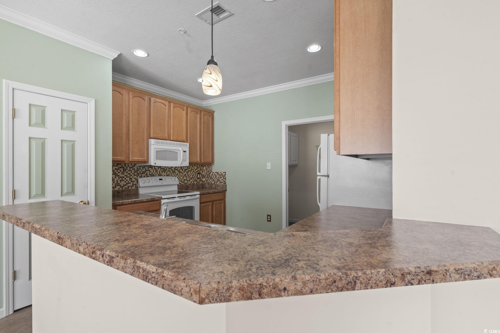 237 Moonglow Circle, Unit 102 Murrells Inlet, SC 29576 - Photo 7 of 35 Kitchen with backsplash, dark countertops, white appliances, crown molding, and pendant lighting