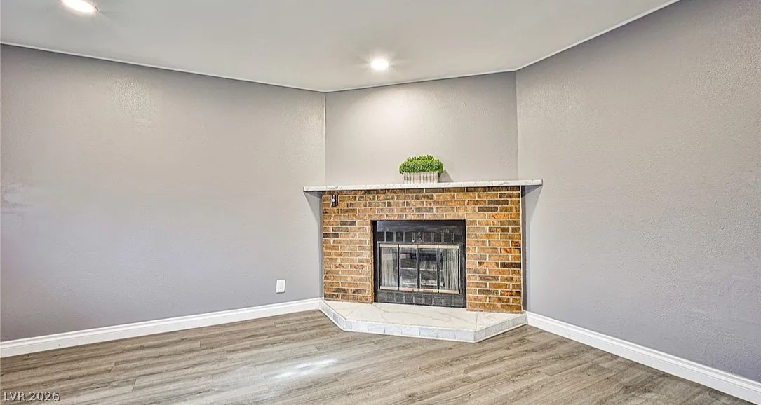 15 Washington Way Henderson, NV 89015 - Photo 6 of 9 Unfurnished living room featuring a textured wall, wood finished floors, a brick fireplace, and recessed lighting