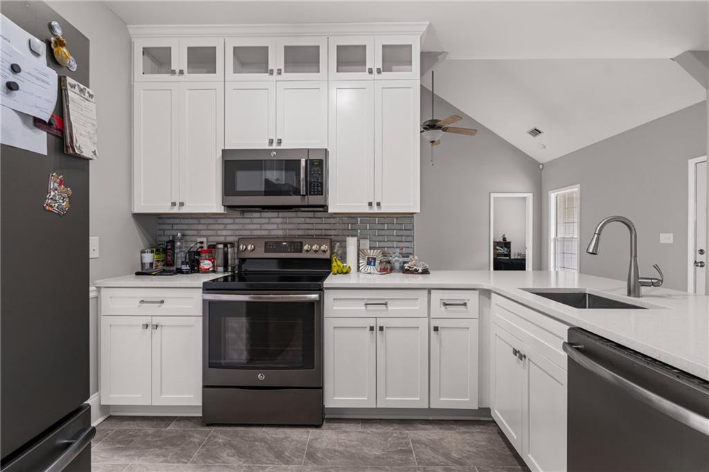 1449 Cummings Road Smiths Station, AL 36877 - Photo 16 of 28 White cabinetry, quartz countertops, stainless steel appliances, tile backsplash, and vaulted ceilings