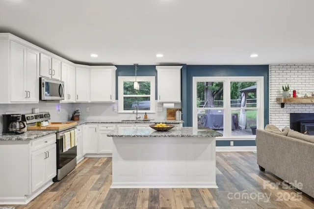 a kitchen with stainless steel appliances granite countertop a stove top oven a refrigerator a sink and dishwasher with wooden floor