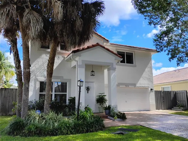 a view of a white house with a small yard plants and a large tree