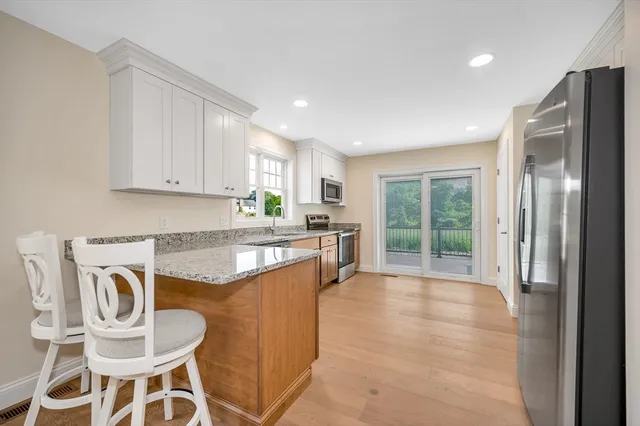a kitchen with granite countertop kitchen island stainless steel appliances a stove a refrigerator a sink a dining table and chairs with wooden floor