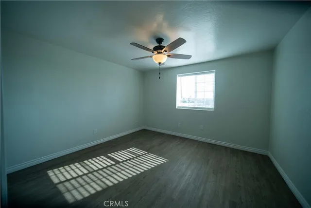 an empty room with wooden floor fan and windows