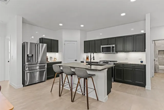 a kitchen with stainless steel appliances granite countertop a stove top oven a refrigerator and a sink with wooden cabinets