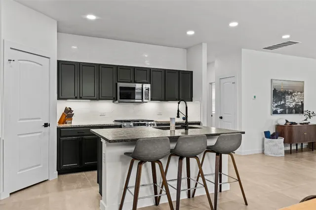 a kitchen with stainless steel appliances a stove top oven a refrigerator a sink and a dining table with chairs