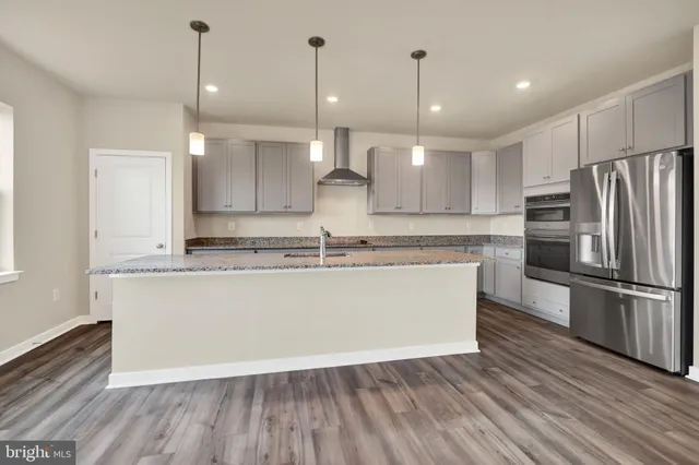 a large kitchen with granite countertop a large counter a refrigerator and wooden floor