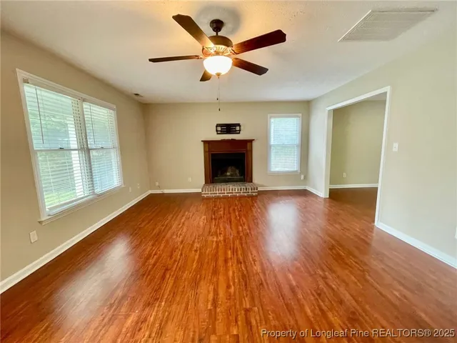 an empty room with wooden floor chandelier fan and windows