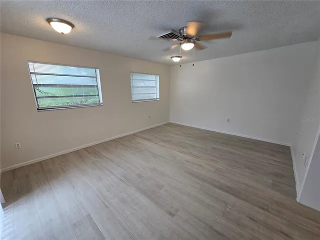 an empty room with wooden floor chandelier fan and windows
