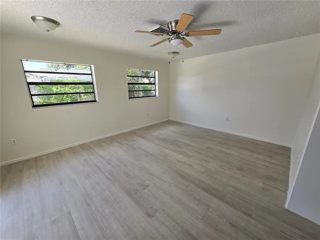 an empty room with wooden floor chandelier fan and windows