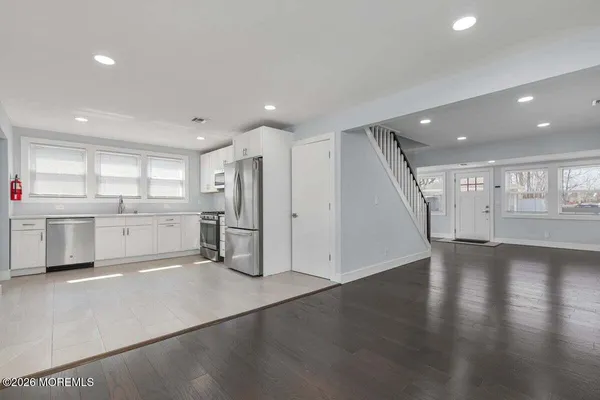 a view of an empty room with wooden floor and a kitchen