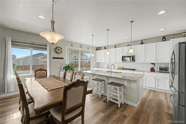 a kitchen with stainless steel appliances a dining table chairs stove a refrigerator a sink a dining table and chairs with wooden floor