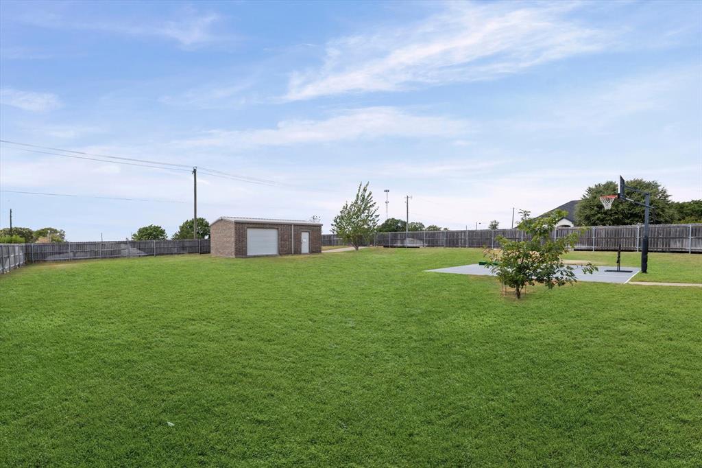 125 Mini Road Lorena, TX 76655 - Photo 32 of 39 Expansive green lawn, brick-finish detached garage with roll-up door, wood privacy fencing, hardscaped sports court, and mature trees