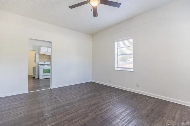 an empty room with wooden floor chandelier fan and windows
