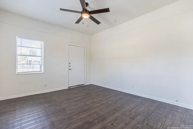 an empty room with wooden floor ceiling fan and windows